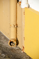 detail of an old iron pipe on a wall painted yellow