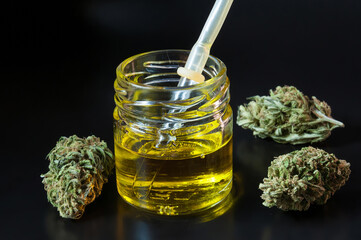 small transparent glass bottle and pipette filled with cannabis oil and dry marijuana flowers...