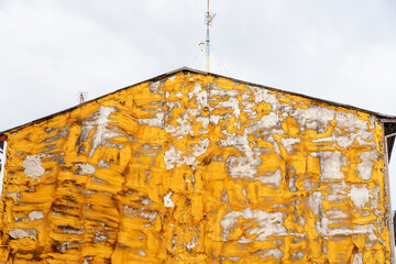 Wall of a residential building with peeling, deteriorating yellow paint.