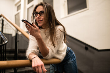 Female on stairs using mobile phone recording voice message during free time in hotel