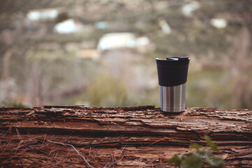 Obraz premium Horizontal shot of a travel mug on a log over blurred nature background with copy advertising space