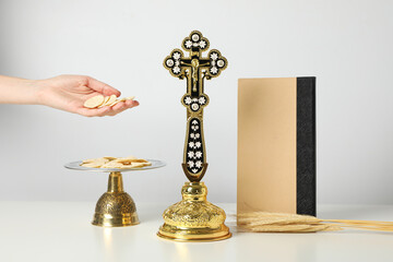 Cross, liturgical bread, hand and book on white background