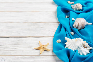 Seashells, blue fabric and starfish on white planks vacation planning background flat lay with...