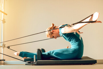 Flexible and slim woman doing stretching exercises on Pilates machine