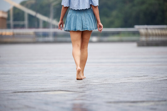 An adult woman in a denim skirt walks barefoot around the city