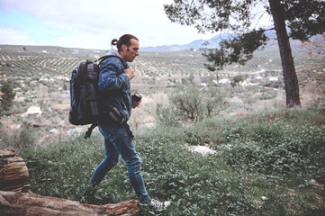 Naklejka premium Young hiker man with backpack and travel mug trekking in the forest over mountains view
