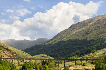 Fototapeta na wymiar The Glenfinnan Viaduct carves a path through the Scottish Highlands, its arches framing the lush greenery, with mountainous terrain rising under a dramatic sky
