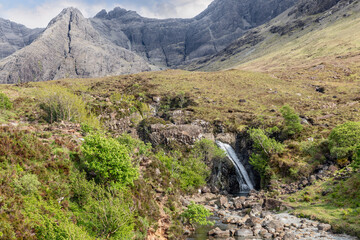 A delicate waterfall descends into the Fairy Pools, framed by the Isle of Skye's lush terrain and...