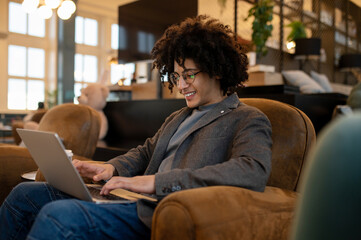 Young smiling curly-haired man spending time online