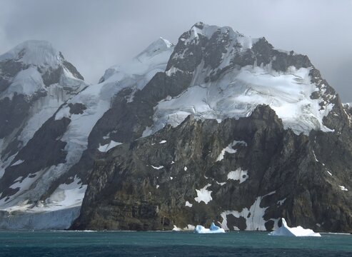approaching the formidable mountain peaks, icebergs,  and glaciers of elephant island,  on the antarctic peninsula, on a  summer cruise on a  stormy day  
