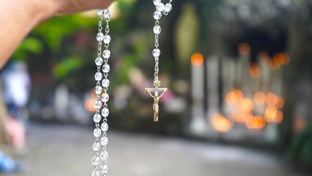 Person praying rosary. Catholic woman holding rosary in hand with candle lights bokeh background.