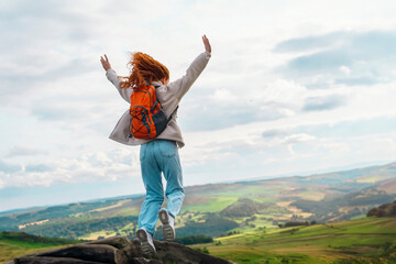 amazing redhead woman with orange backpack raising her hands, jumping, reaching the destination and...