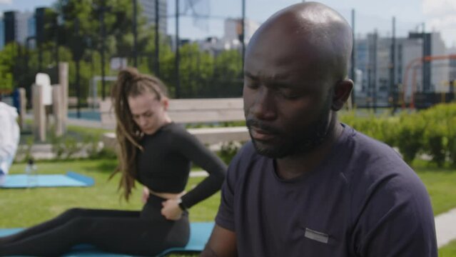 Side chest up footage of young African American man warming up his neck while turning head on outdoor training in park