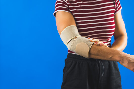 woman wearing elastic support elbow brace for reduce pain, blue background. High quality photo