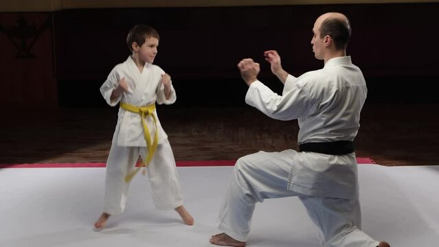A child athlete with a yellow belt trains punches on the palms of the trainer