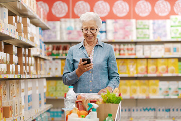 Happy senior woman buying groceries and using a smartphone