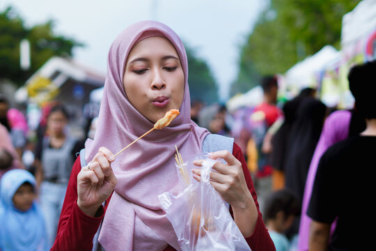 woman in hijab eating cilor or telor gulung, Indonesian street food concept.