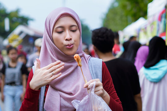 woman in hijab eating cilor or telor gulung, Indonesian street food concept.