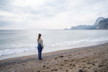 Back side view of a girl stands on the seashore, young woman is looking into the distance, before...