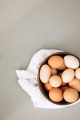 Chicken eggs of different brown and beige shades in a large wooden bowl on a grey background with white kitchen towel. Easter background. Top view