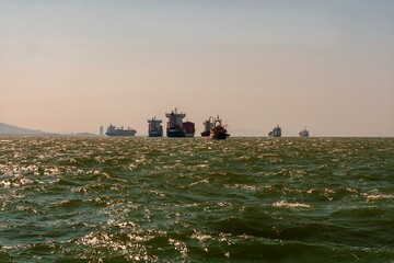 Cargo ships and their traffic moving and waiting in the bay on the green wavy sea