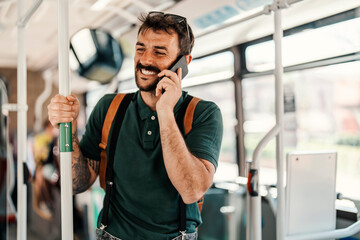 Portrait of a happy young man standing in a city bus and commuting while talking on the phone.