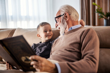A grandfather is reading book and fairytale to his grandchild at home.
