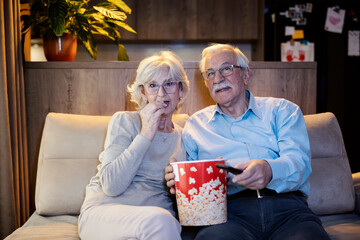 A senior couple is watching movies at home and eating popcorn.