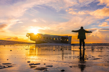 Young adventurous man at sunrise on Solheimasandur plane in winter in Iceland, with open arms