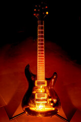 A black electric guitar with chrome tone control knobs on a stand standing on the floor enlightened...