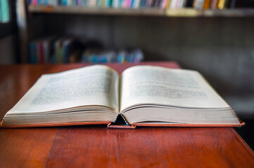 An open book or textbook vintage style on wooden table in the library and the bookshelves background.Education learning concept