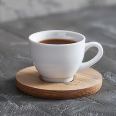 a white ceramic cup filled with coffee. placed on a round wooden coaster that showcases visible natural grain patterns. The background is textured and grey in color