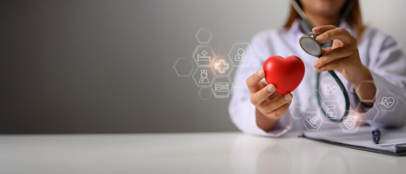 Hands of female cardiologist holding stethoscope examining red heart. Health insurance and cardiology concept