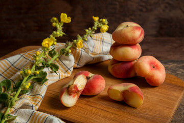 Cutting board with halves and several whole saturn peaches or flat peaches on wooden background...