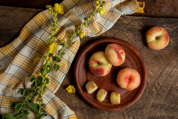 Clay plate with cut and whole saturn peaches or flat peaches on wooden background with yellow kitchen towel.. © kostik2photo