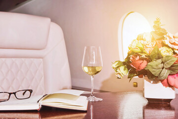 Comfort vip salon private business jet with flowers, diary, wine, eyeglasses on table. Luxury decor...