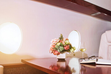 Comfort vip business salon private jet with flowers, diary, wine glass, glasses on table. Luxury...