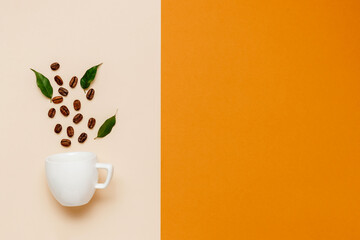  White coffee cup with coffee beans and green leaves on beige and orange background with copy space...