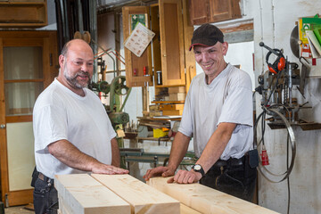 Tischler und sein Mitarbeiter begutachten das gehobelte Holz in der Werkstatt - 756348621