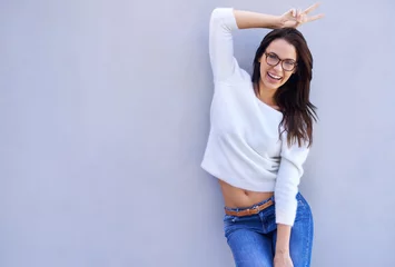 Foto op Plexiglas Portrait, fashion and smile with bunny ears woman on wall background for comedy, fun or humor. Style, glasses and hand gesture with confident young person in trendy or casual clothing outfit © peopleimages.com
