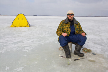 A man fishes on the ice of a lake. A fishing tent stands on the ice of a lake. © Sergei