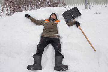 A man with a shovel lies in the snow.