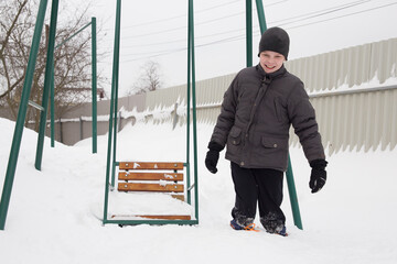 a boy stands knee-deep in the snow near a children's swing.