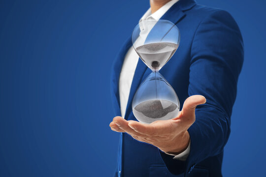 Businessman holding an hourglass isolated on blue background.