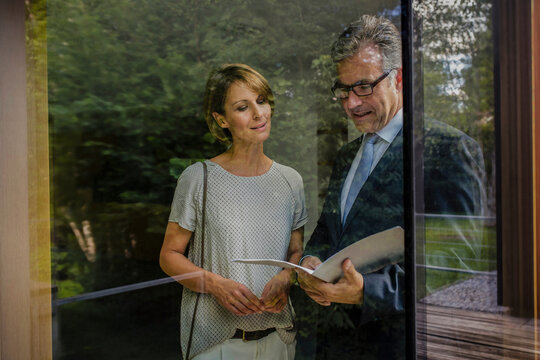 Frau  mit Immobilienmakler schauen Vertragsunterlagen an einer neuen Immobilie, Blick durch ein Fenster, Bayern, Deutschland