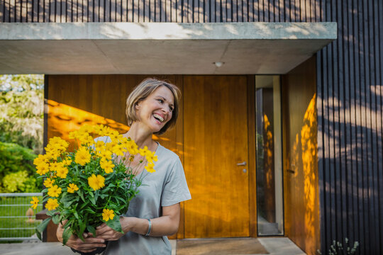 gl&uuml;ckliches Frau mit Blumenstrauss vor einer neuen Immobilie, Bayern, Deutschland