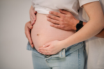 Cropped image of husband holding  hands belly of his pregnant wife. Pregnant woman and loving handsome man hugging tummy at home. Loving Couple. Parenthood concept. Baby Shower.