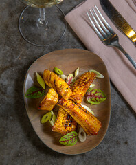 Side view of a chef gourmet plate of corn cob and salad. Black modern restaurant table. 