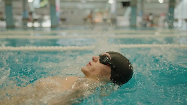 Closeup of man in goggles swimming backstroke in pool. Male swimmer training in swimming pool. Sport concept