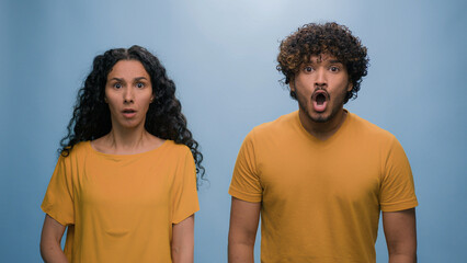 Hispanic Indian Arabian couple at blue studio background shocked bad news terrible shock amazed...